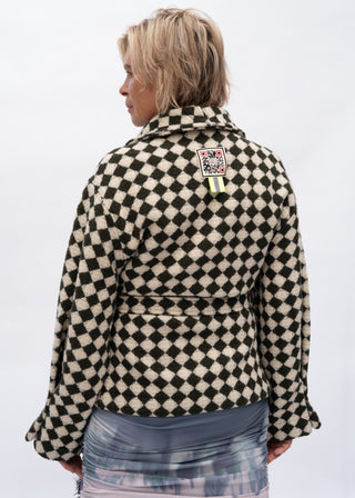 A model shown from the back wearing a black and cream checkered jacket with a high collar and a small colorful patch on the upper back, set against a plain white background.