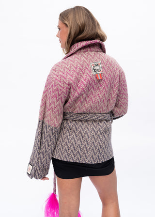 A woman shown from the back wearing a pink and gray chevron-patterned wrap jacket with a matching tie belt, paired with a black mini skirt. The jacket features a pink upper section and a gray lower section with a zigzag pattern.
