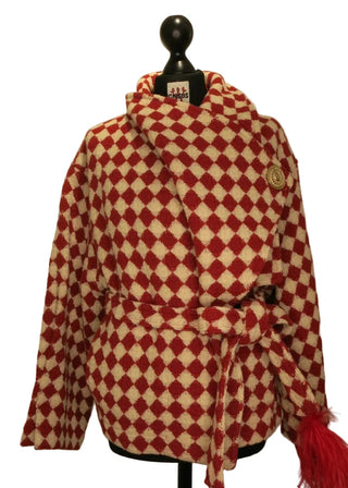A red and cream diamond-patterned coat with red tassels, displayed on a black mannequin against a plain beige background.