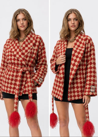 A model is shown in a split-screen view wearing a red and beige checkered wrap coat with a tie belt and fluffy red tassels, styled over a black dress.