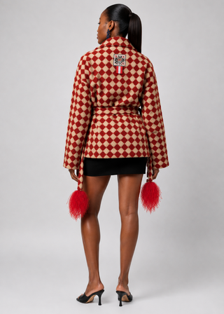 A model shown from the back wearing a red and beige diamond-patterned jacket with red feather accents at the cuffs, paired with a black mini skirt and black heels, against a light gray studio background.