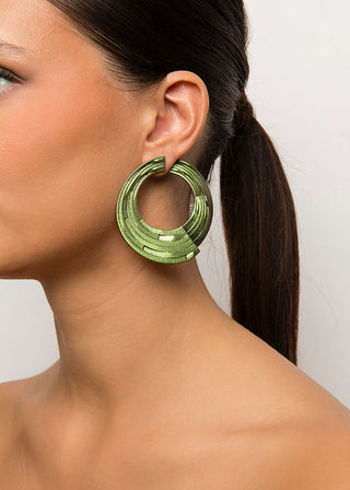 Close-up of a woman wearing a green hoop earring against a neutral background