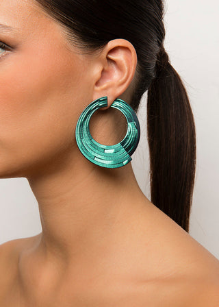 Close-up of a woman wearing a green hoop earring with a plain background