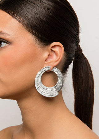 Close-up of a woman wearing silver hoop earrings with a neutral background
