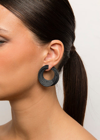 Close-up of a woman wearing a black hoop earring with a plain background