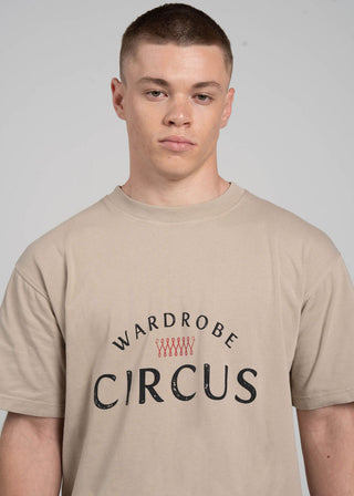 Person wearing a beige t-shirt with 'Wardrobe Circus' text on a plain background