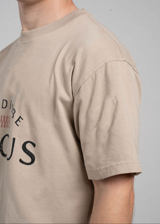 Beige t-shirt with text worn by a person on a plain background