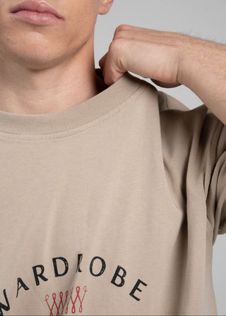 Person wearing a beige t-shirt with 'WARDROBE CIRCUS' branding on a plain background