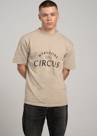 Man wearing a beige t-shirt with 'Wardrobe Circus' text on a plain background