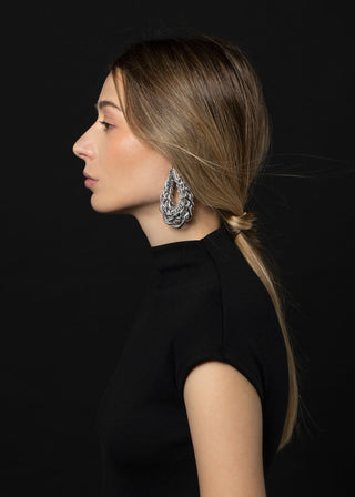 Woman wearing a black dress and silver earrings against a black background
