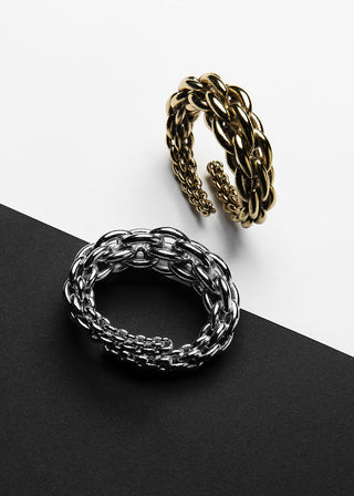 Two chunky chain-link wrap rings, one in polished silver and one in antique gold, displayed on a diagonal split black and white background.