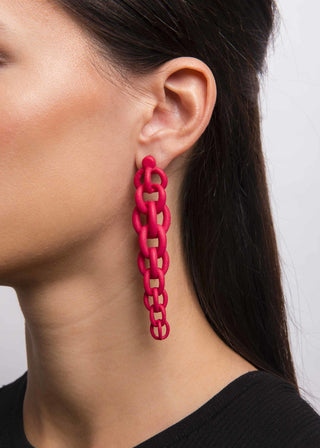 Close-up of a person wearing bright red chain-link earrings against a neutral background