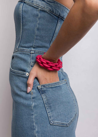 Person wearing blue jeans with a pink bracelet on a plain background