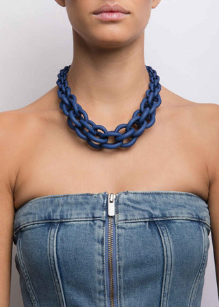 Person wearing a blue chain necklace with a denim top against a plain background