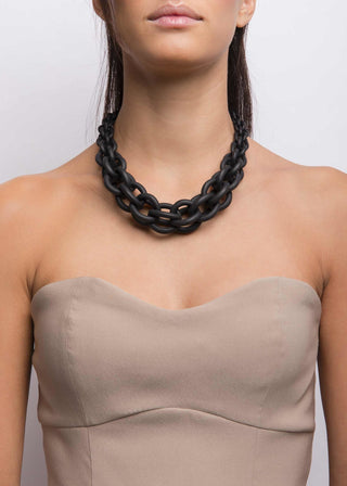 Woman wearing a black chain necklace against a plain background