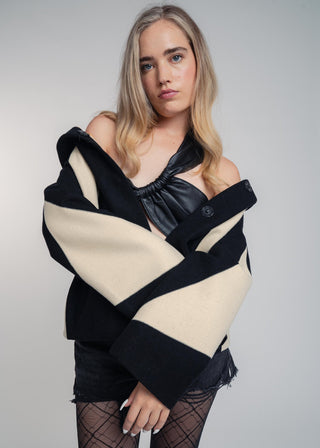 Woman wearing a black and beige off-shoulder jacket against a plain background