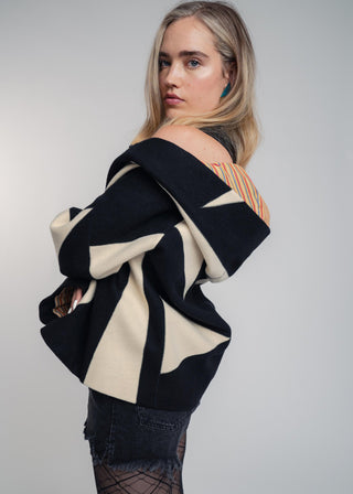 Woman wearing a black and beige off-shoulder jacket against a plain background