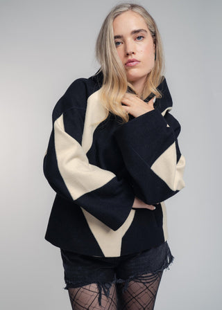 Woman wearing a black and beige geometric patterned jacket on a gray background