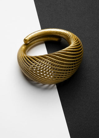 A textured gold-toned metal cuff ring with a twisted, ribbed design, photographed on a split white and black background.