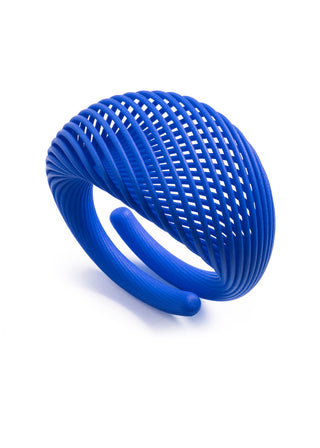 A vibrant blue sculptural ring with a dense, open lattice or mesh pattern, photographed on a clean white background.