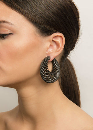 Close-up of a woman wearing a gunmetal colored spiral earring with a neutral background