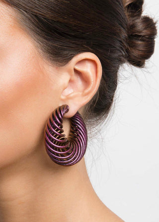 Close-up of a woman wearing mermaid purple spiral earrings with a plain background