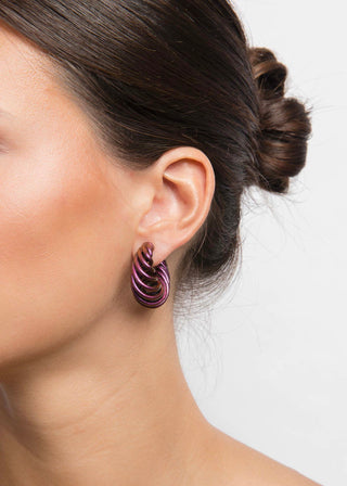 Close-up of a person wearing a mermaid purple spiral earring on a plain background