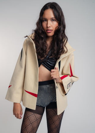 Woman wearing a beige jacket with red accents, black leather top, and patterned skirt on a plain background