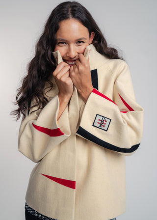 Woman wearing a cream-colored jacket with red and black accents on a plain background