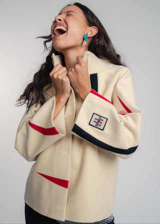 Woman wearing a cream-colored jacket with red and black accents on a plain background