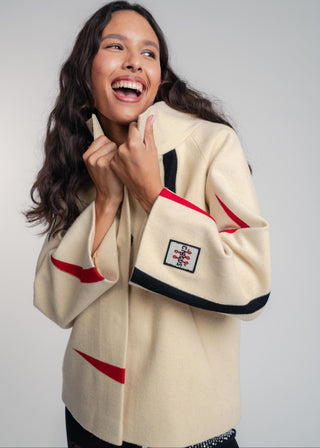 Woman wearing a beige jacket with red and black accents on a plain background