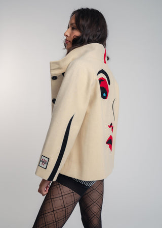 Person wearing a beige jacket with colorful designs on a plain background