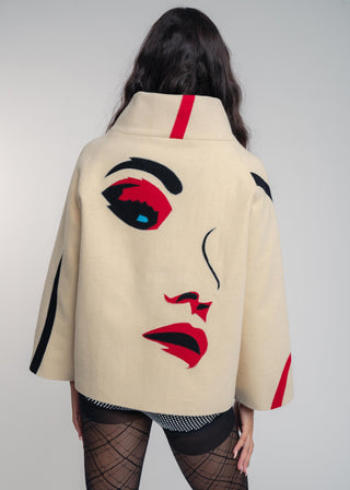 Beige coat with artistic face design worn by a person on a gray background