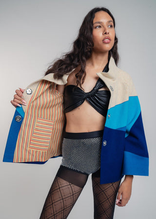 Woman wearing a colorful jacket with a patterned interior, black top, and fishnet stockings on a gray background.