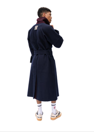 A man wearing a long navy blue coat with a dark burgundy collar, shown from the back and side against a plain white background.