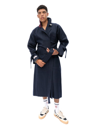 A model wearing a dark navy blue wrap-style coat with a belted waist, styled with white socks and beige sneakers, set against a plain white background.