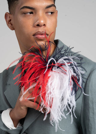 Man wearing a gray suit with a colorful feathered accessory around his neck against a plain background
