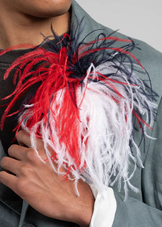 Feathered accessory with red, navy, and white feathers held by a person wearing a gray jacket.