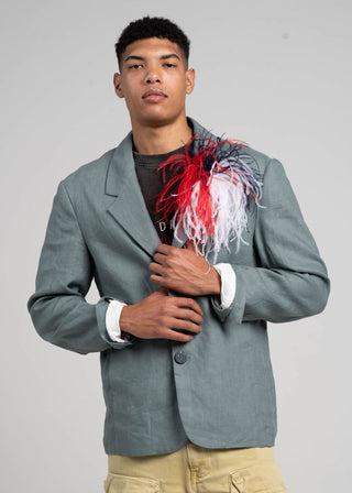 Man wearing a gray blazer with a colorful brooch, standing against a plain background