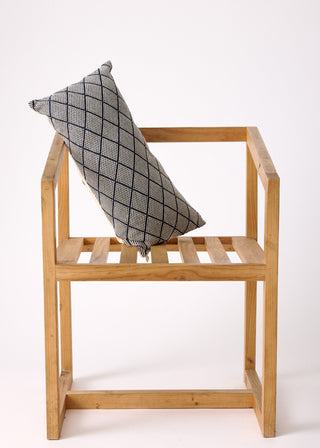 A rectangular pillow case with a diamond pattern on a wooden stool, with a natural horn button finish.