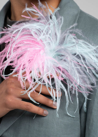 Person wearing a gray coat with a decorative pink and white feathered accessory.