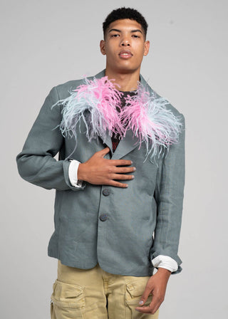 Person wearing a gray blazer with pink and white feather accents on a plain background