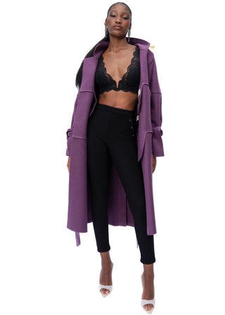 A model wearing a long purple open-front coat over a black lace bralette and black leggings, standing against a plain white background.