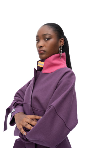 A model wearing a purple oversized coat with a contrasting hot pink collar, photographed against a solid white background.