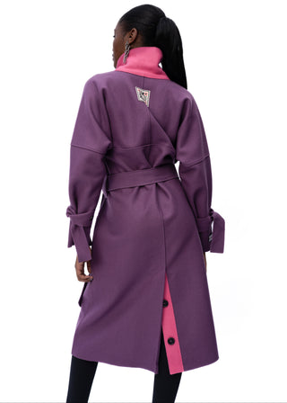 A model shown from the back wearing a mid-length purple wrap-style coat with a bright pink collar and inner back lining, photographed against a plain white background.