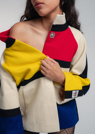 Person wearing a colorful jacket with red, yellow, blue, and beige sections on a plain background