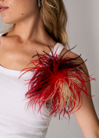 A close-up of a model wearing a white ribbed tank top and a dramatic red and black feathered shoulder embellishment.