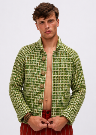 A male model wearing a green and white patterned cropped jacket with wooden buttons, paired with red striped pants, against a plain light gray background.