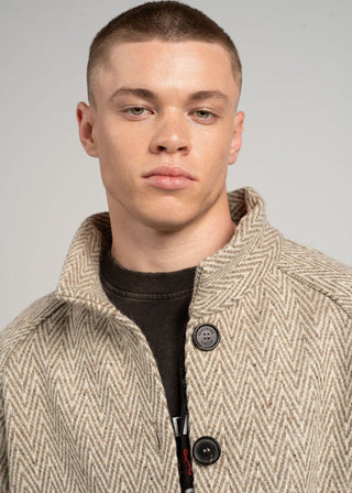 Man wearing a beige herringbone coat against a gray background