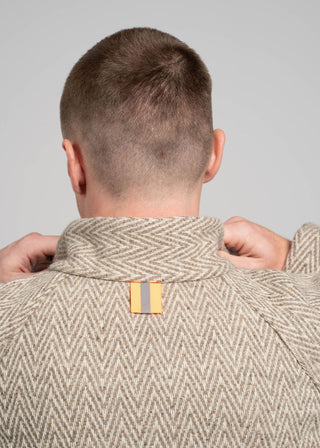 Person wearing a beige herringbone patterned jacket with a visible brand logo on a gray background